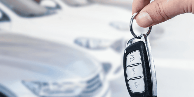 Mano sostiene las llaves de un coche, con vehículos de fondo