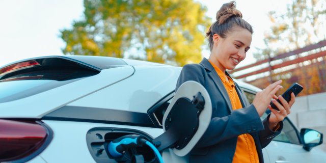 Mujer revisa su celular con un vehículo eléctrico a su espalda