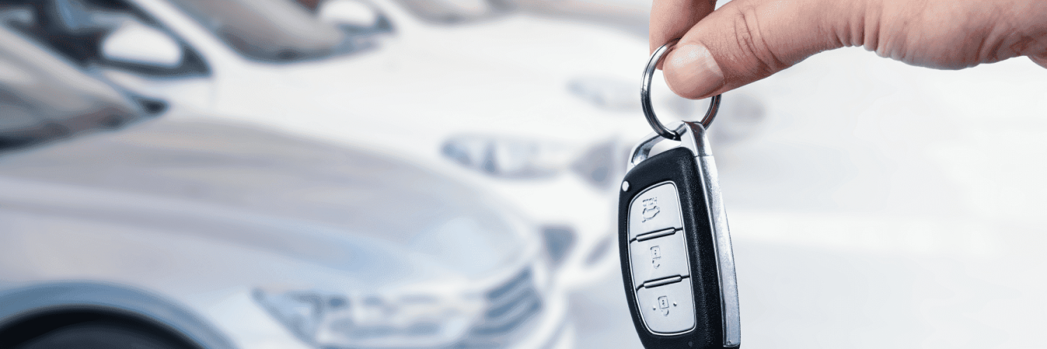 Mano sostiene las llaves de un coche, con vehículos de fondo